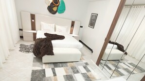A modern bedroom with a bed, bedside tables, a desk, and a wall-mounted air conditioner. - Charming 1-bedroom apartment with AC, Power backup  and Dishwasher in  Kampala (Kampala)