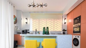 A modern kitchen with a central island, bar stools, a built-in oven, and a washing machine. - Charming 1-bedroom apartment with AC, Power backup  and Dishwasher in  Kampala (Kampala)