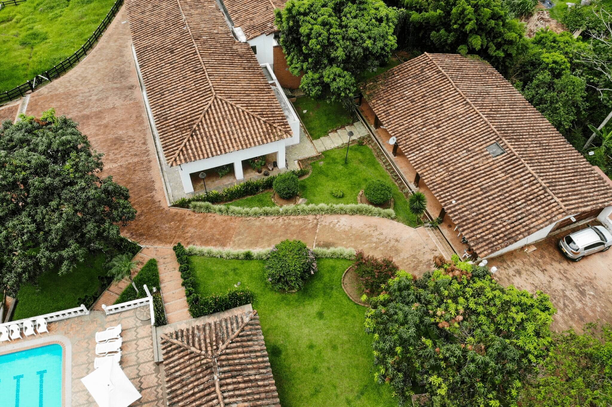 An aerial view of a residential area with terracotta-roofed houses, a swimming pool, and well-maintained gardens.