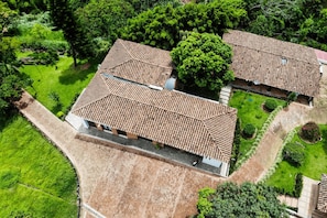 Vista aérea de uma propriedade com vários edifícios e telhados de terracota, cercada por vegetação exuberante e jardins bem cuidados.