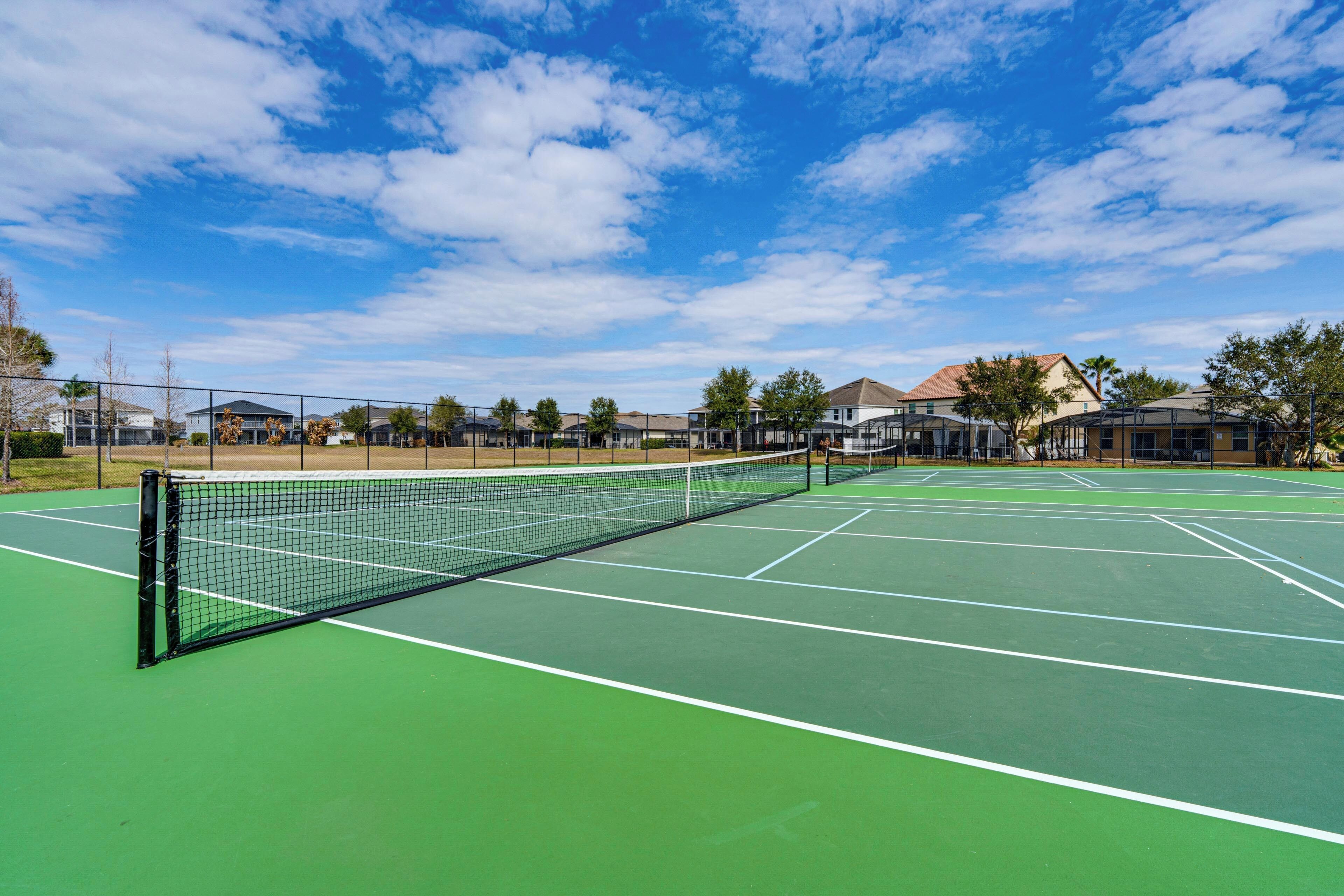 A tennis court with a net, surrounded by buildings and trees.