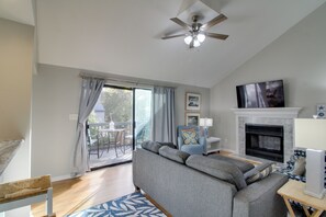 A living room with a grey sofa, a TV mounted above a fireplace, and a ceiling fan. - Sun, Surf & Sand in Fort Walton Beach! Cozy Condo (Fort Walton Beach)
