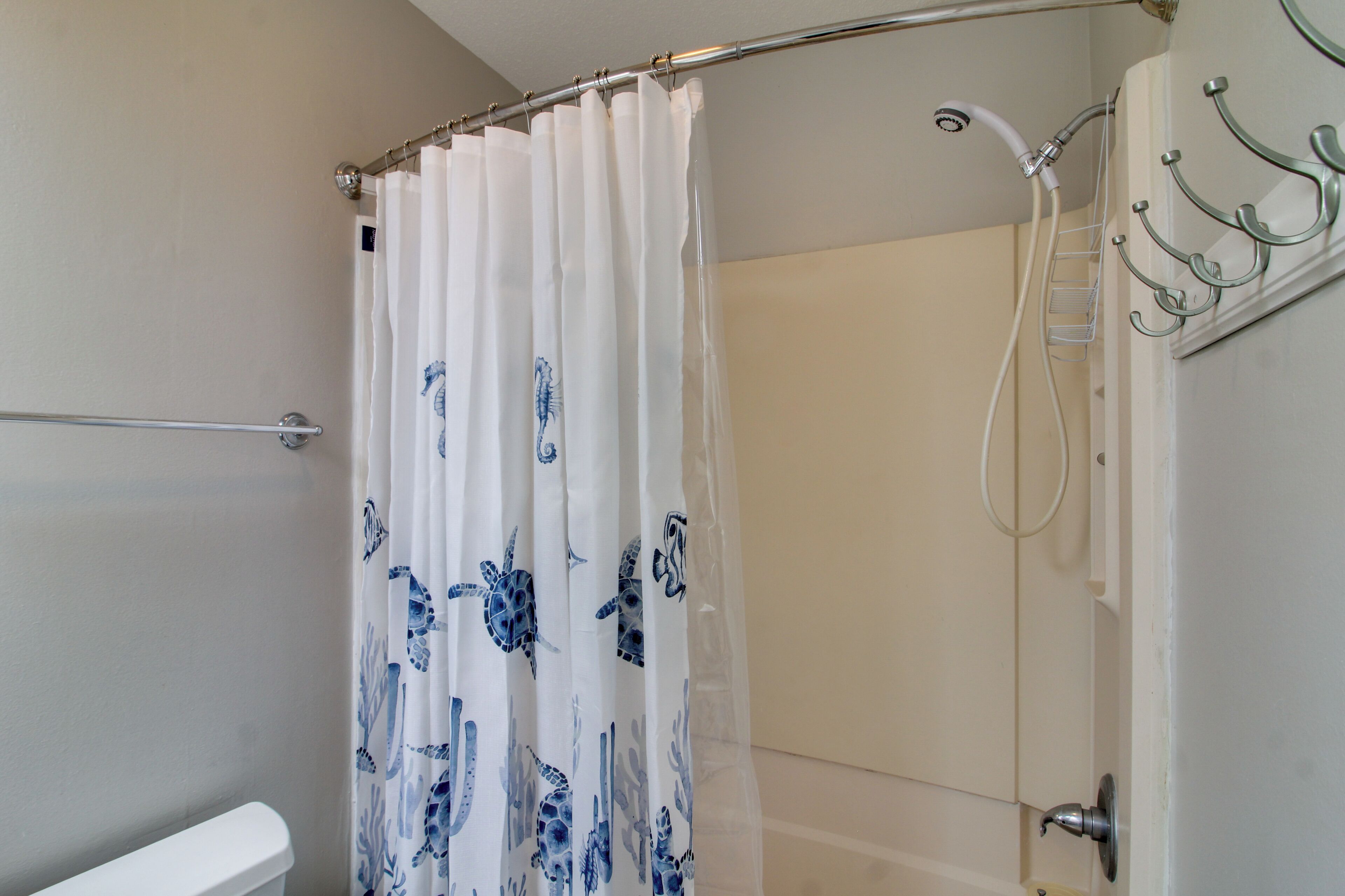 A shower area with a white shower curtain featuring blue sea turtle patterns, a glass shower door, and a metal towel rack.