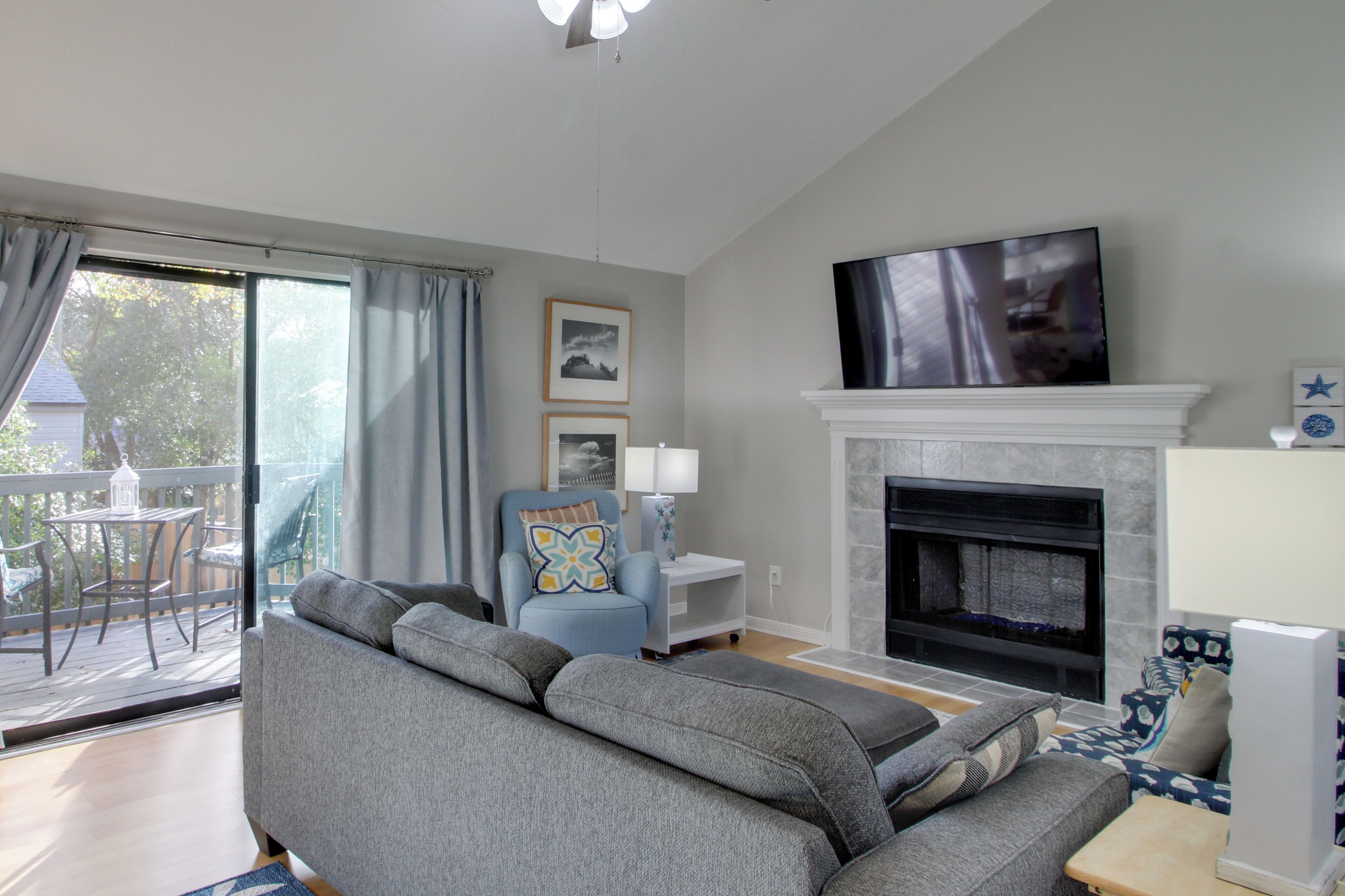 A living room with a grey sofa, a blue armchair, a fireplace, and a TV mounted above it.