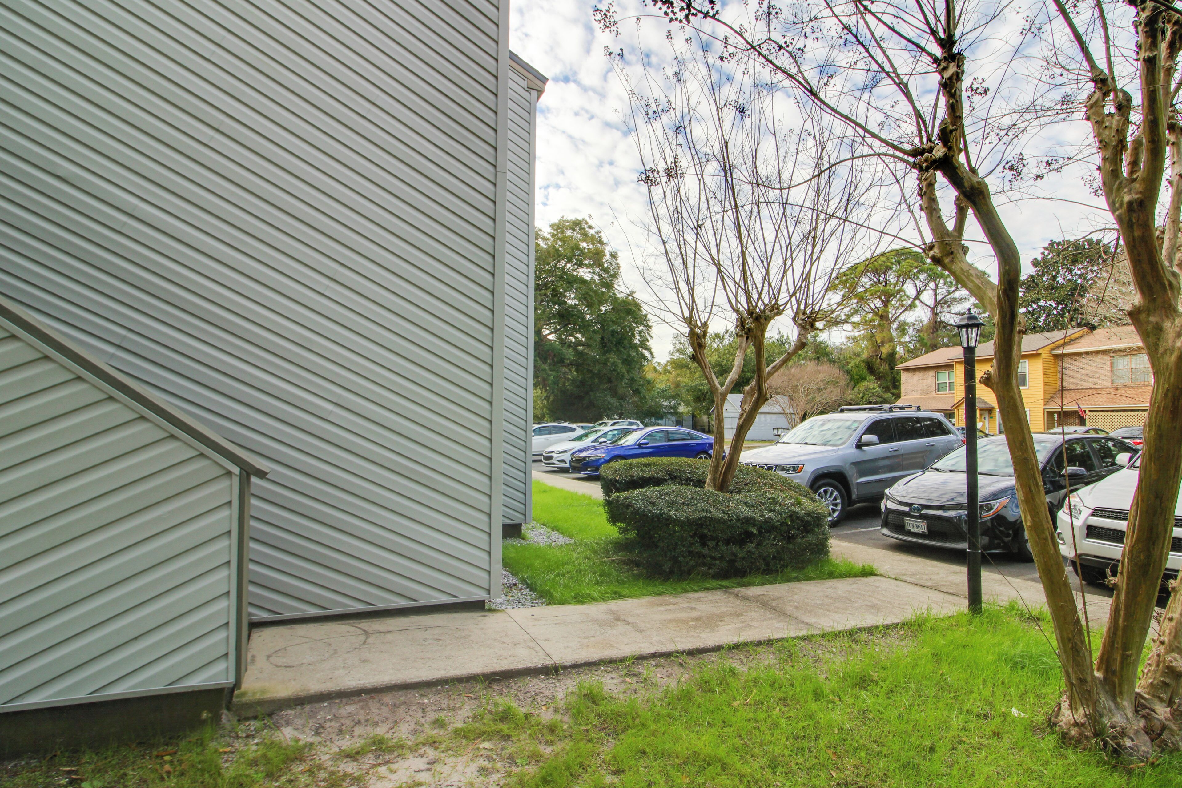 A residential building with a sloped roof, a parking lot with several cars, and a small bush in the foreground.