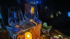 A wooden table with a variety of cheeses, meats, and olives, accompanied by two glasses and a candle.
