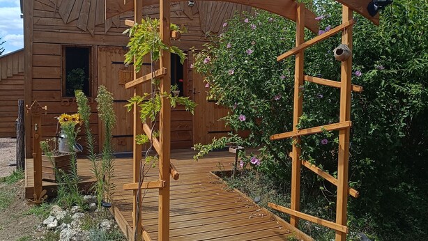 A wooden pergola with a wooden deck leading to a rustic wooden building.