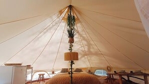 A tent with a bed, a lamp, a small table, and a basket.