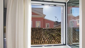 Una ventana con vista a un tejado de tejas y un edificio de fachada rosa.