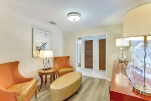 Habitación de hotel con zona de estar que incluye dos sillones y una mesita, una lámpara decorativa y una obra de arte enmarcada en la pared.