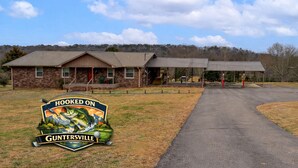 A building with a porch, a covered area, and a sign with a fishing theme. - Spacious Fishing Getaway by Lake Guntersville! (Scottsboro)
