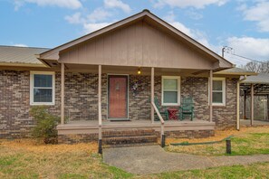 A two-story house with a brick facade, a front porch with steps, and a red door. - Spacious Fishing Getaway by Lake Guntersville! (Scottsboro)