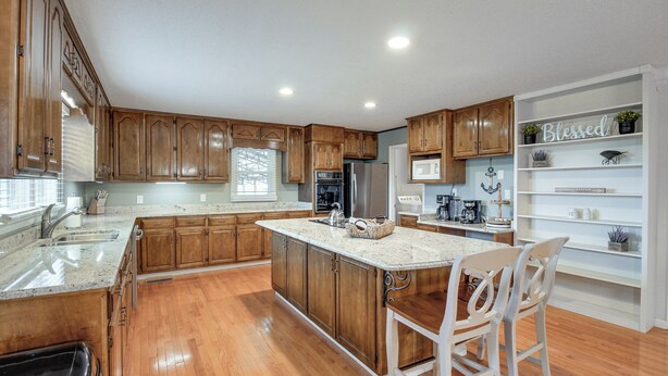 A kitchen with wooden cabinets, a marble countertop, and a built-in island with bar stools. - Spacious Fishing Getaway by Lake Guntersville! (Scottsboro)