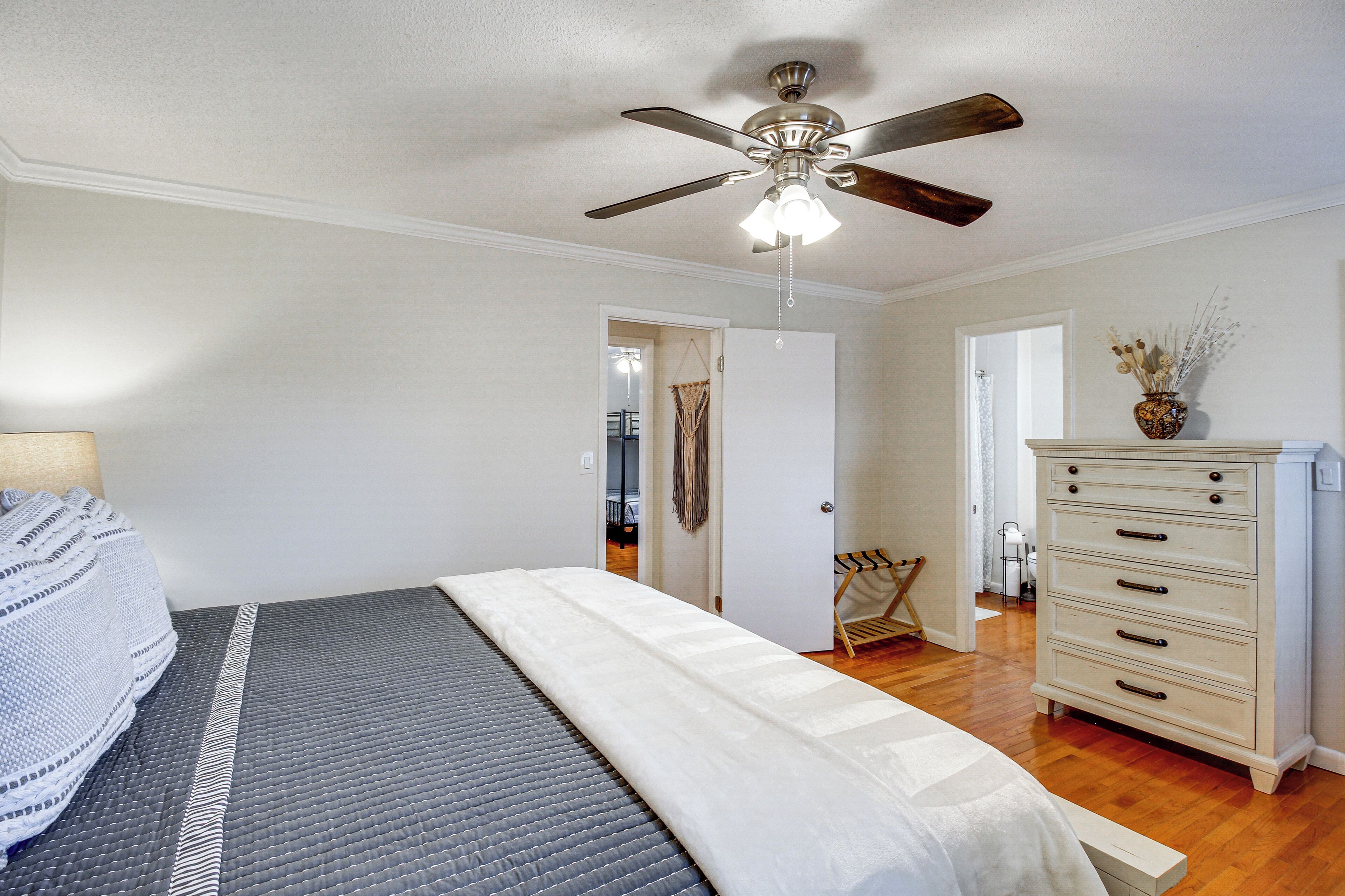 A bedroom with a bed, a dresser, a ceiling fan, and a door leading to another room.
