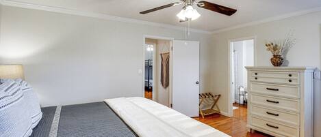 A bedroom with a bed, a dresser, a ceiling fan, and a door leading to another room.