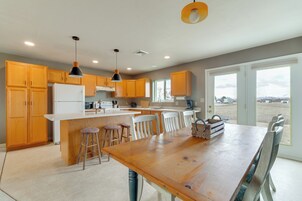 A modern kitchen with wooden cabinets, a central island with stools, and a large dining table.