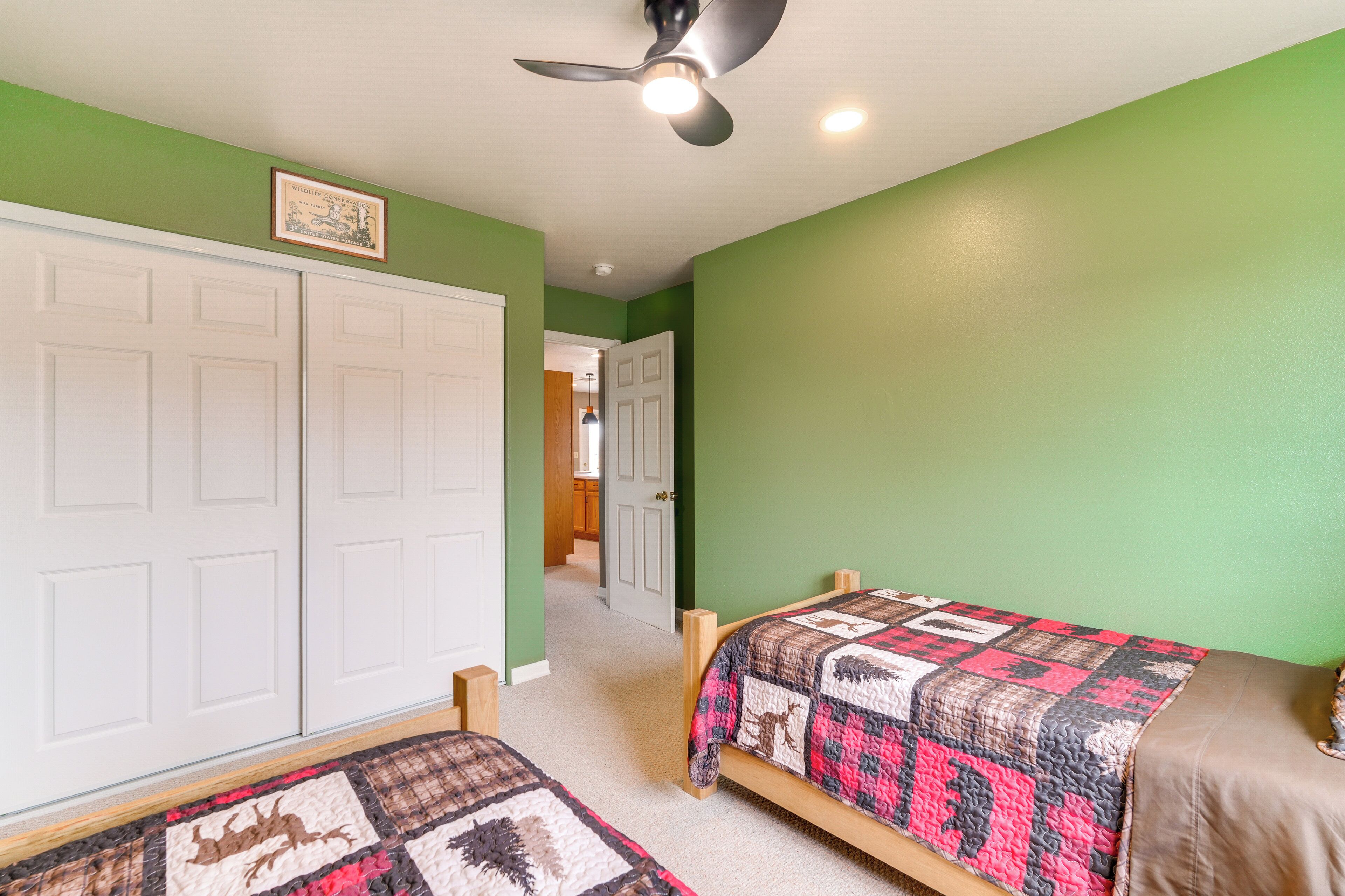 A bedroom with two beds, a ceiling fan, and a door leading to another room.