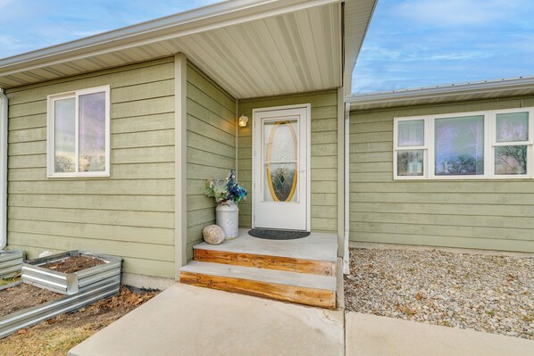 A house with a front porch, a door with a glass panel, and a small garden area with steps leading up to the door. - Hike, Fish & Golf! Pet-friendly Home in Choteau (Choteau)