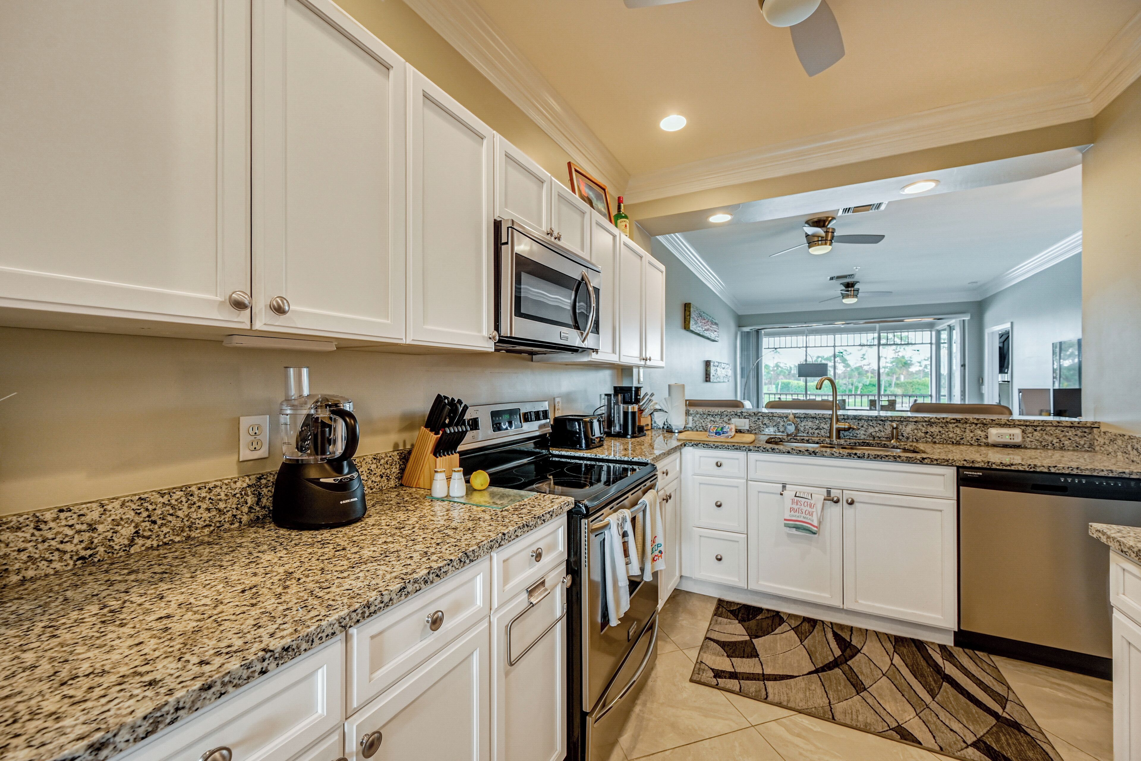 A modern kitchen with granite countertops, white cabinetry, stainless steel appliances, and a large window providing natural light.
