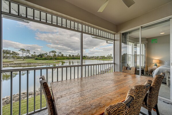 A dining area with a large table and wicker chairs, overlooking a lake with a golf course and trees. - Luxury Waterfront Living! Naples Resort Condo (Naples)