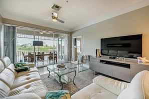 Ein modernes Wohnzimmer mit Sofa, Couchtisch und Fernseher. Ein Balkon bietet Blick ins Freie.