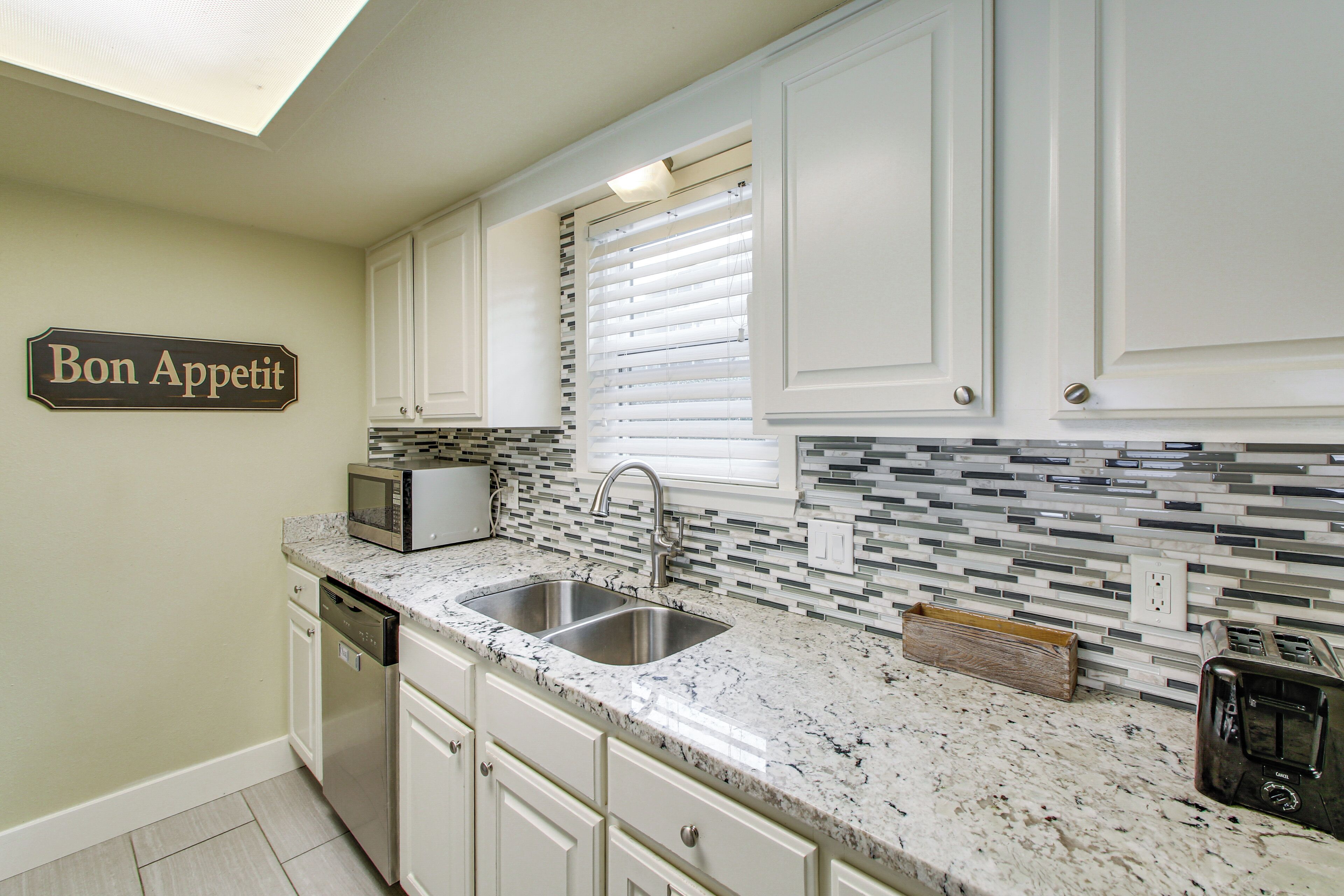 A kitchen with white cabinets, a double sink, a microwave, a toaster, and a sign that reads "Bon Appetit".