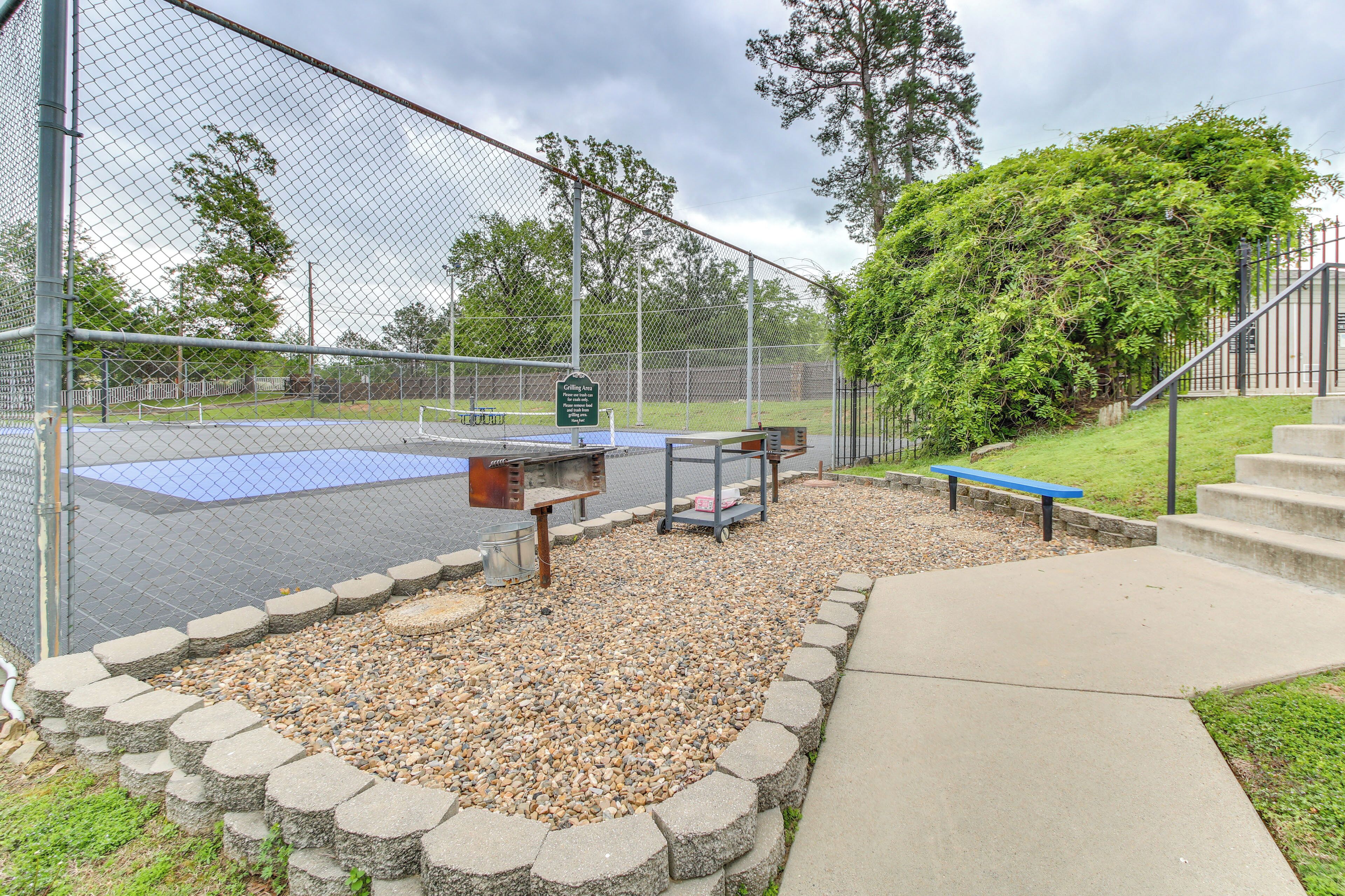 Cancha de tenis cercada con una mesa de picnic y bancos, rodeada por un borde de piedra y una zona verde.