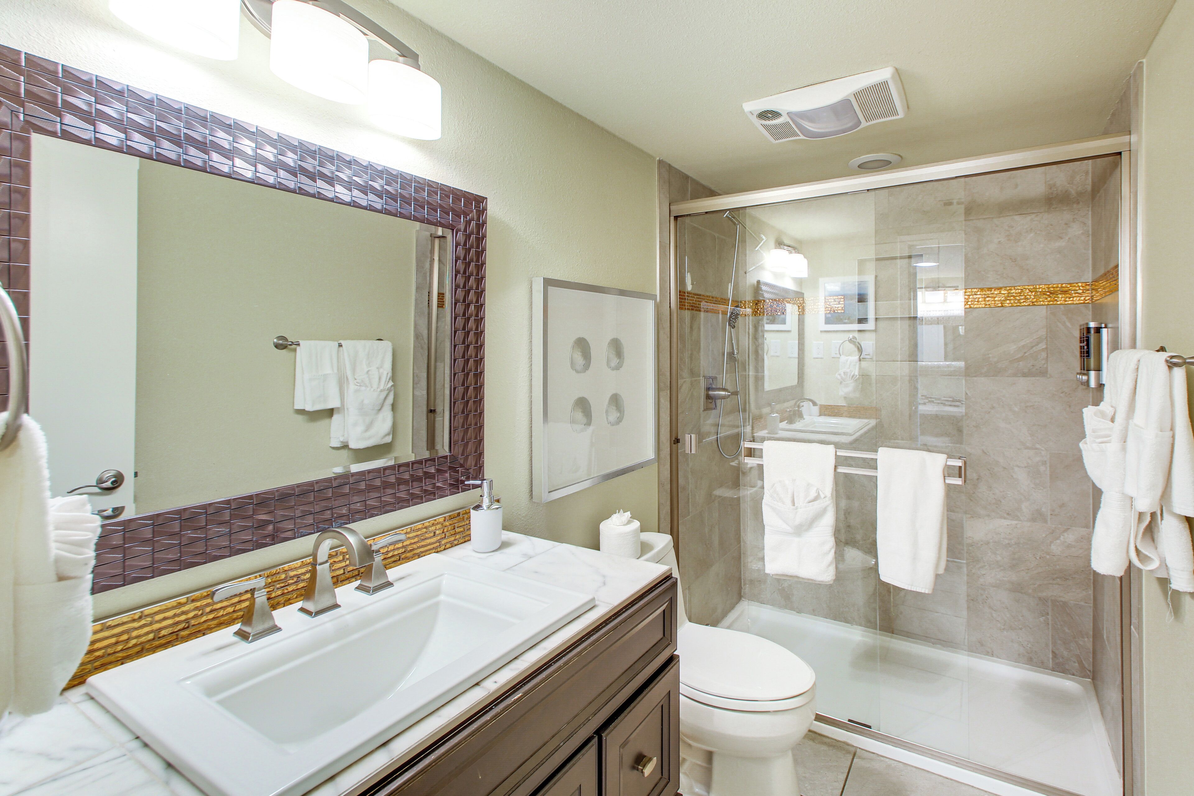 A modern bathroom with a large sink, mirror, and glass shower enclosure.
