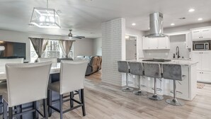 A modern kitchen with white cabinets, a stainless steel range hood, and a central island with bar stools. - Group Getaway Near Eufaula Lake & Boat Ramp! (Eufaula)
