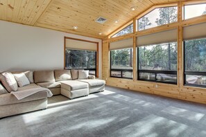 Una sala de estar moderna con un sofá modular, ventanas amplias y techo de madera.