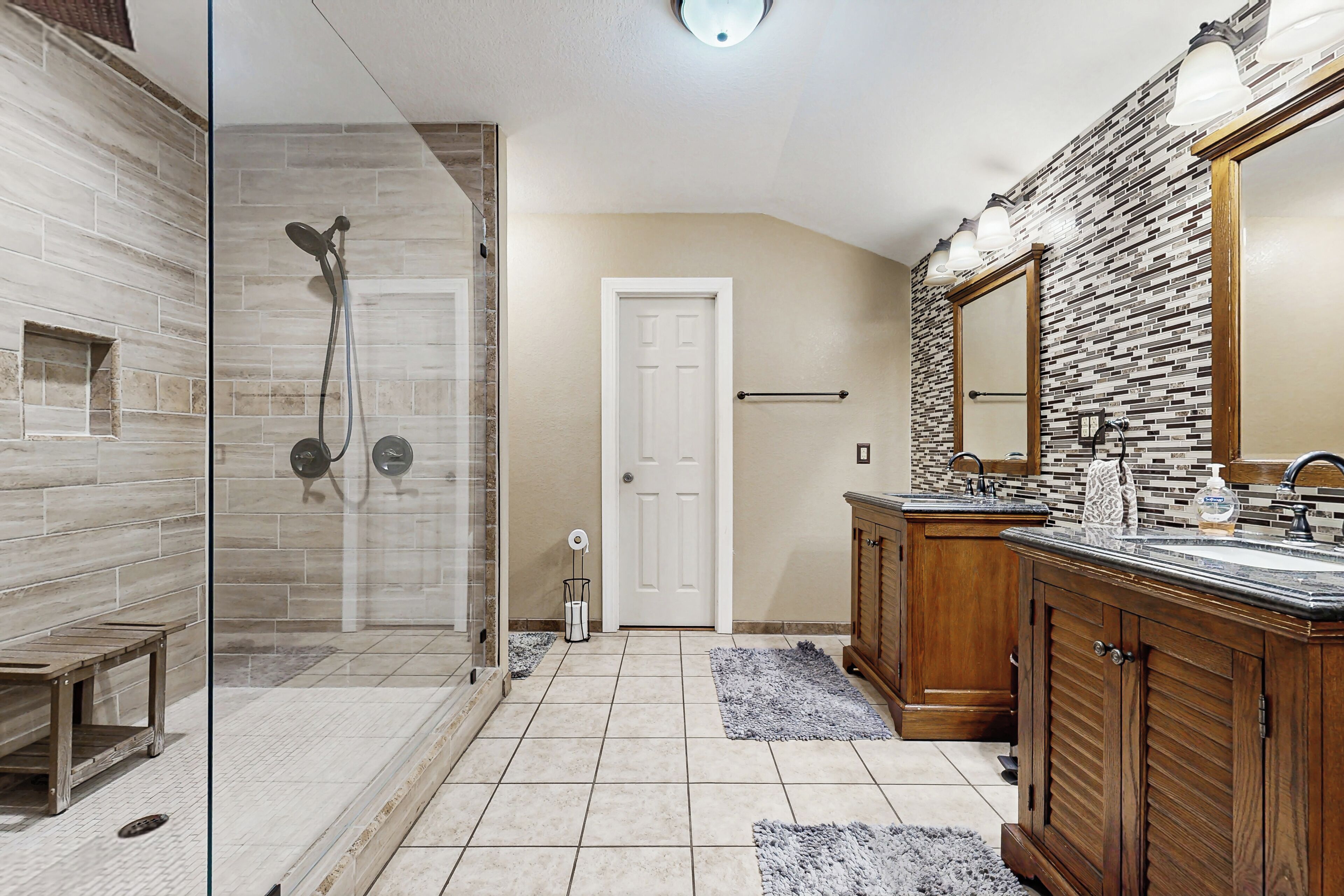 A bathroom with a glass-enclosed shower, wooden vanity, and a tiled floor.
