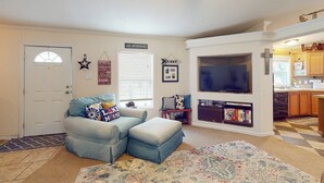 Un salon comprenant un canapé, un pouf et un téléviseur fixé au mur, au-dessus d’une bibliothèque.