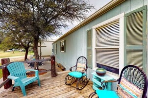 Una terraza de madera con mobiliario exterior, incluyendo sillas y una mecedora, cerca de un edificio con contraventanas.