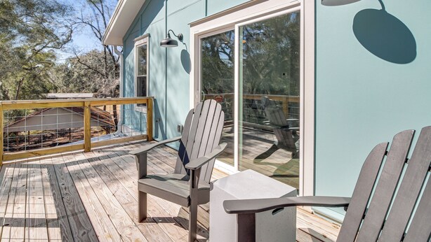 Une terrasse avec des fauteuils Adirondack et une table, d’où l’on peut admirer une maison dotée de grandes fenêtres et d’une façade bleu clair.