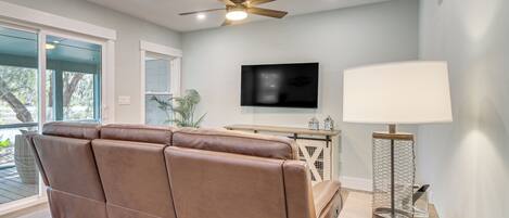 A modern living room with a brown leather sofa, a ceiling fan, a flat-screen TV, and a table lamp.