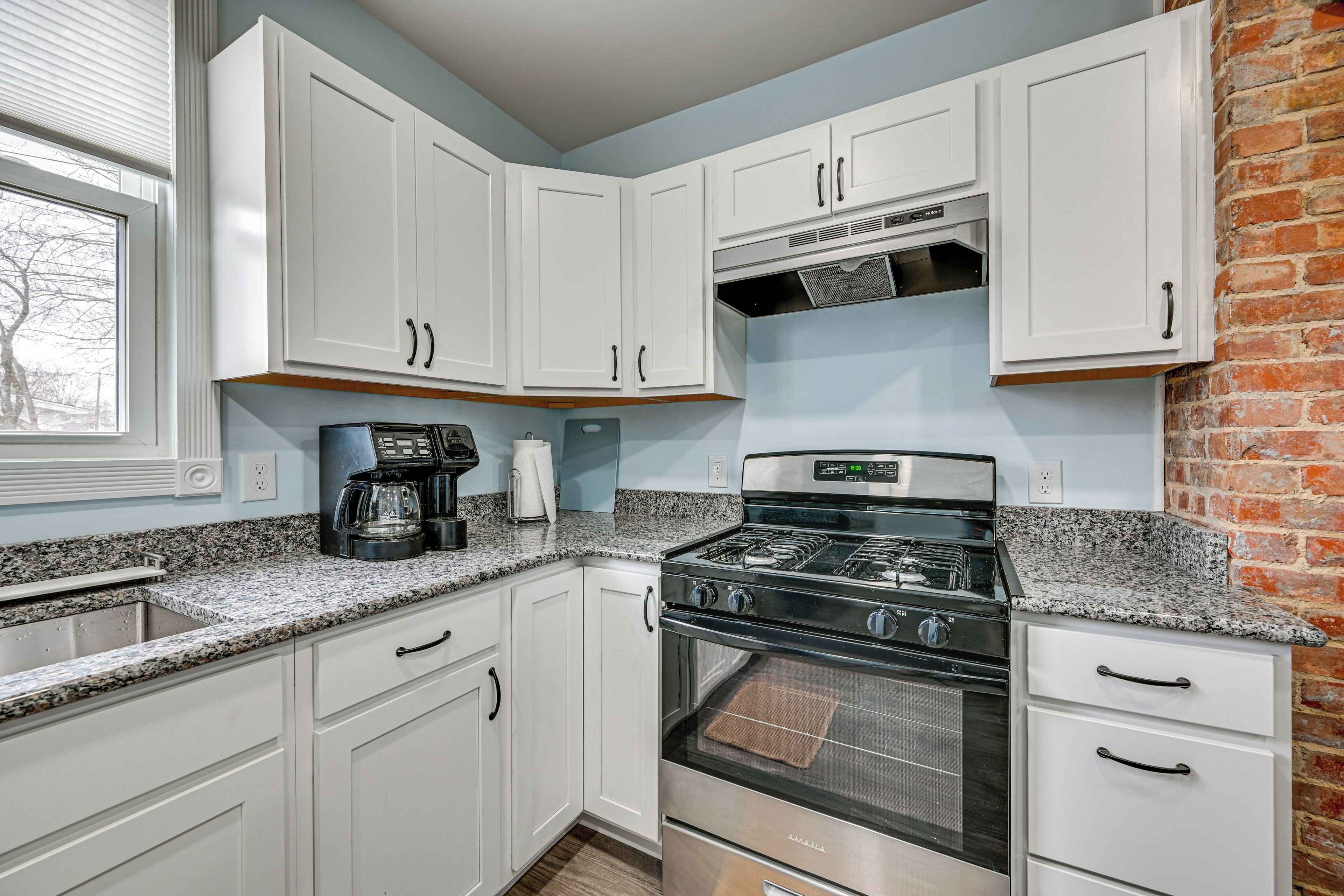 A kitchen with white cabinets, a granite countertop, a stove, and a brick wall.