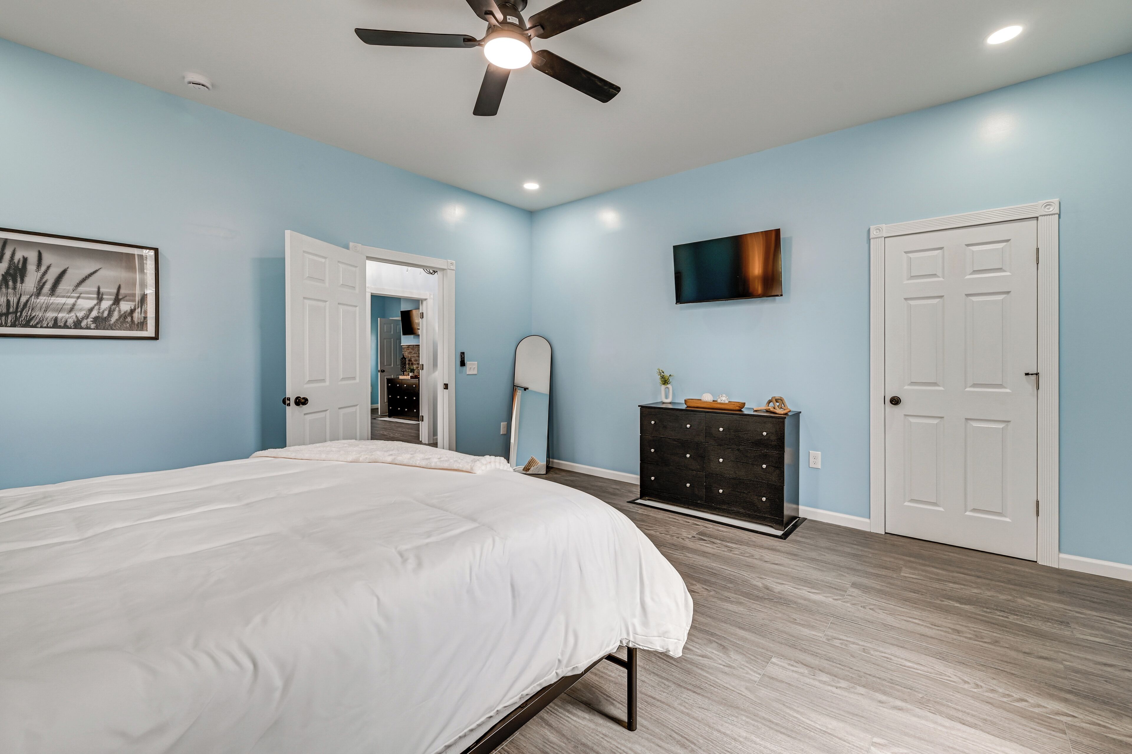 A bedroom with a bed, a ceiling fan, a TV, a dresser, and a door.