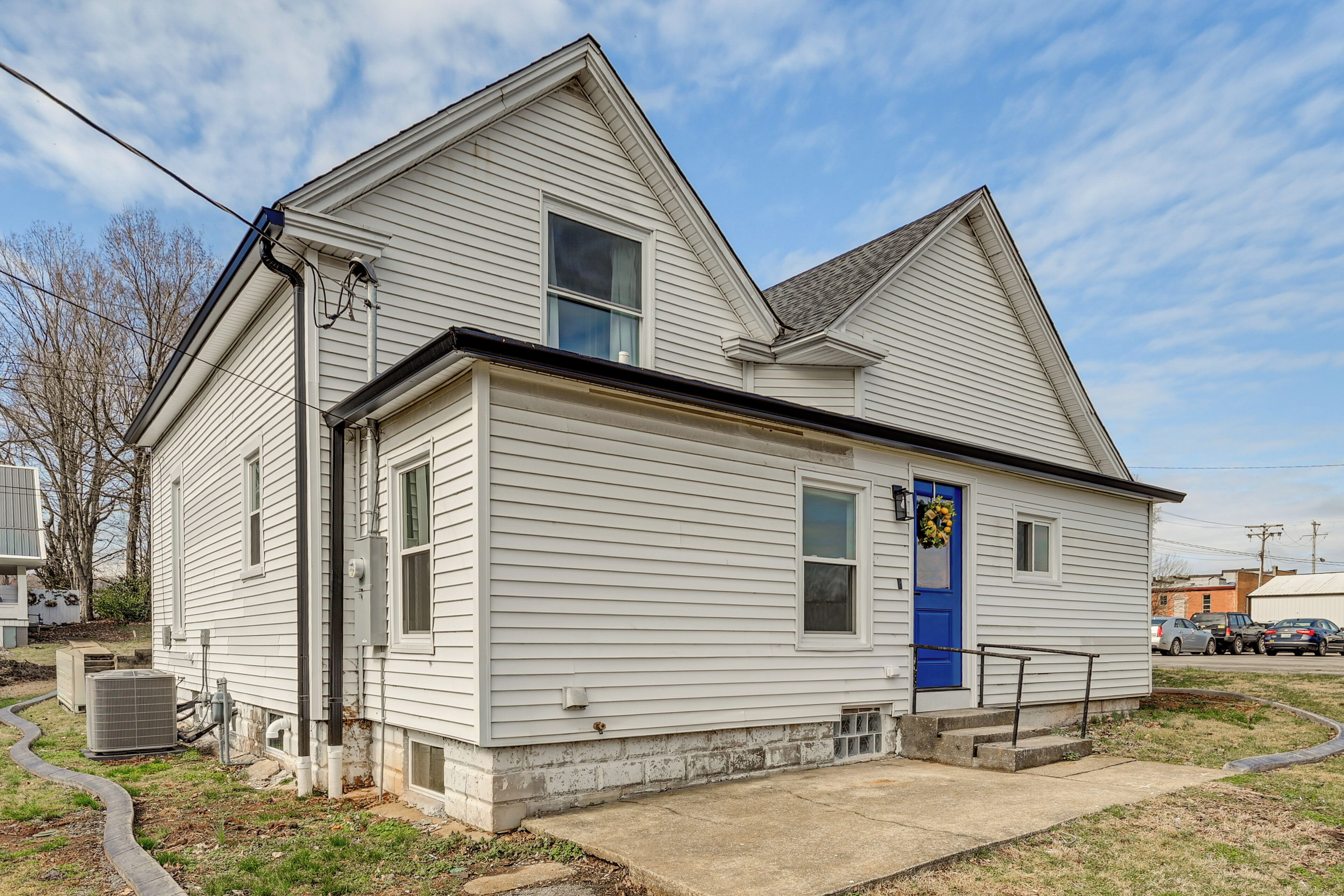 A white single-story house with a blue front door, a small porch, and a visible air conditioning unit.
