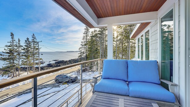 A balcony with a wooden ceiling, a blue cushioned seating area, and a view of a snowy landscape with trees and a body of water. - < 1 Mi to Port Clyde Village: Modern Retreat (Tenants Harbor)