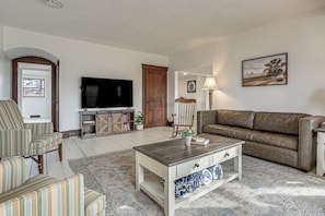 Ein Wohnzimmer mit Sofa, Sessel, Couchtisch, Fernseher und einem Bild an der Wand.