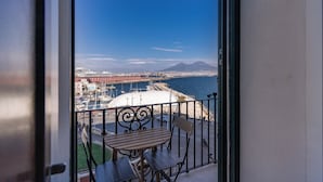 Een balkon met een tafel en stoelen, met uitzicht op een kustgebied met gebouwen en een berg.