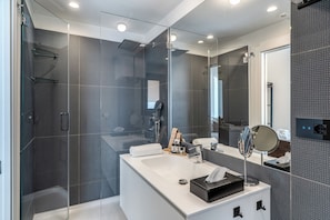 A modern bathroom with a glass-enclosed shower, a white sink with a black soap dish, and a large mirror. - Sette Stelle Suites (Naples)