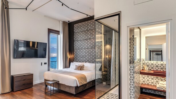 Een moderne slaapkamer met een groot bed, een televisie, een houten vloer en een badkamer met een geometrisch tegelpatroon.