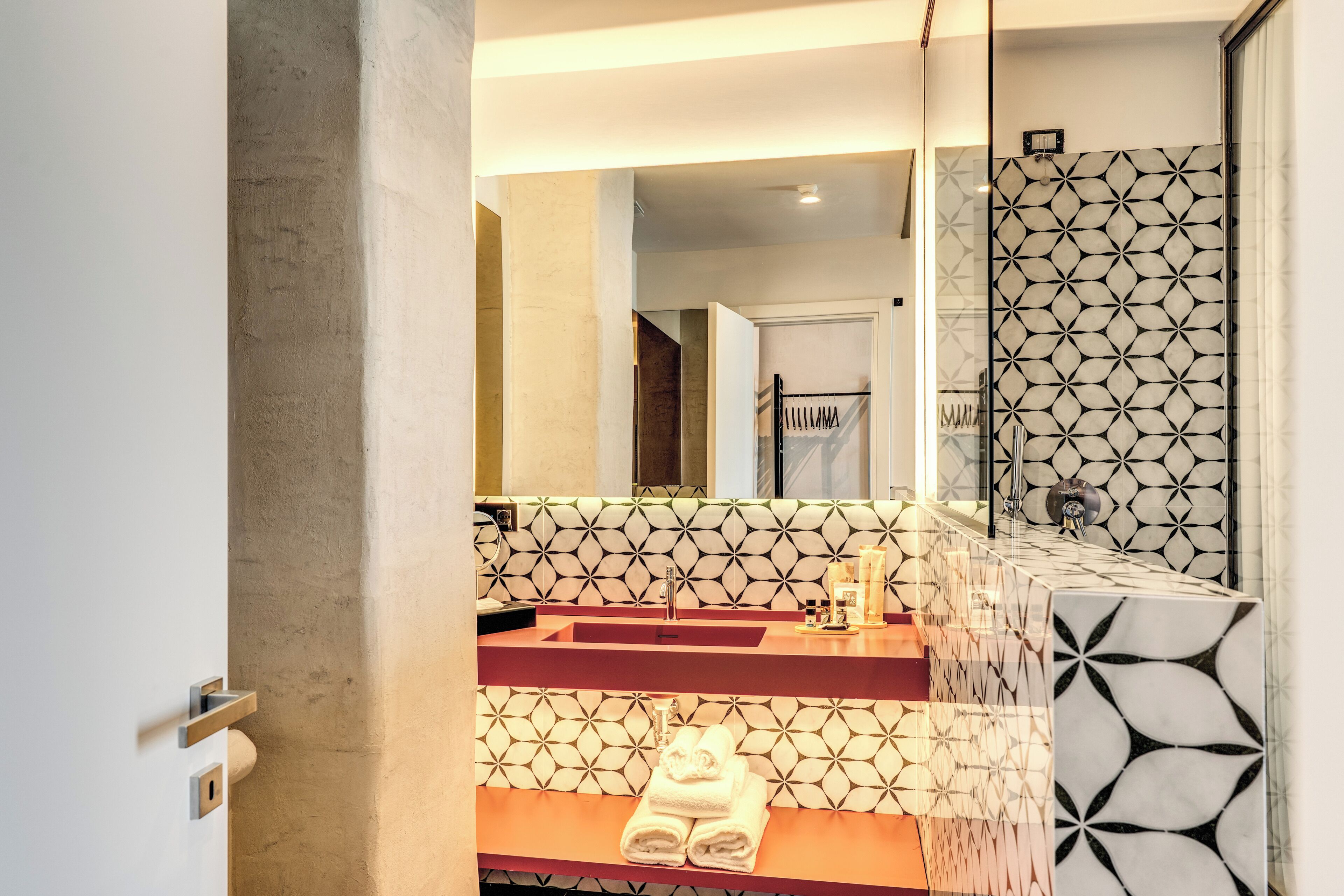 A modern bathroom with a geometric tile backsplash, a red countertop, and a large mirror.