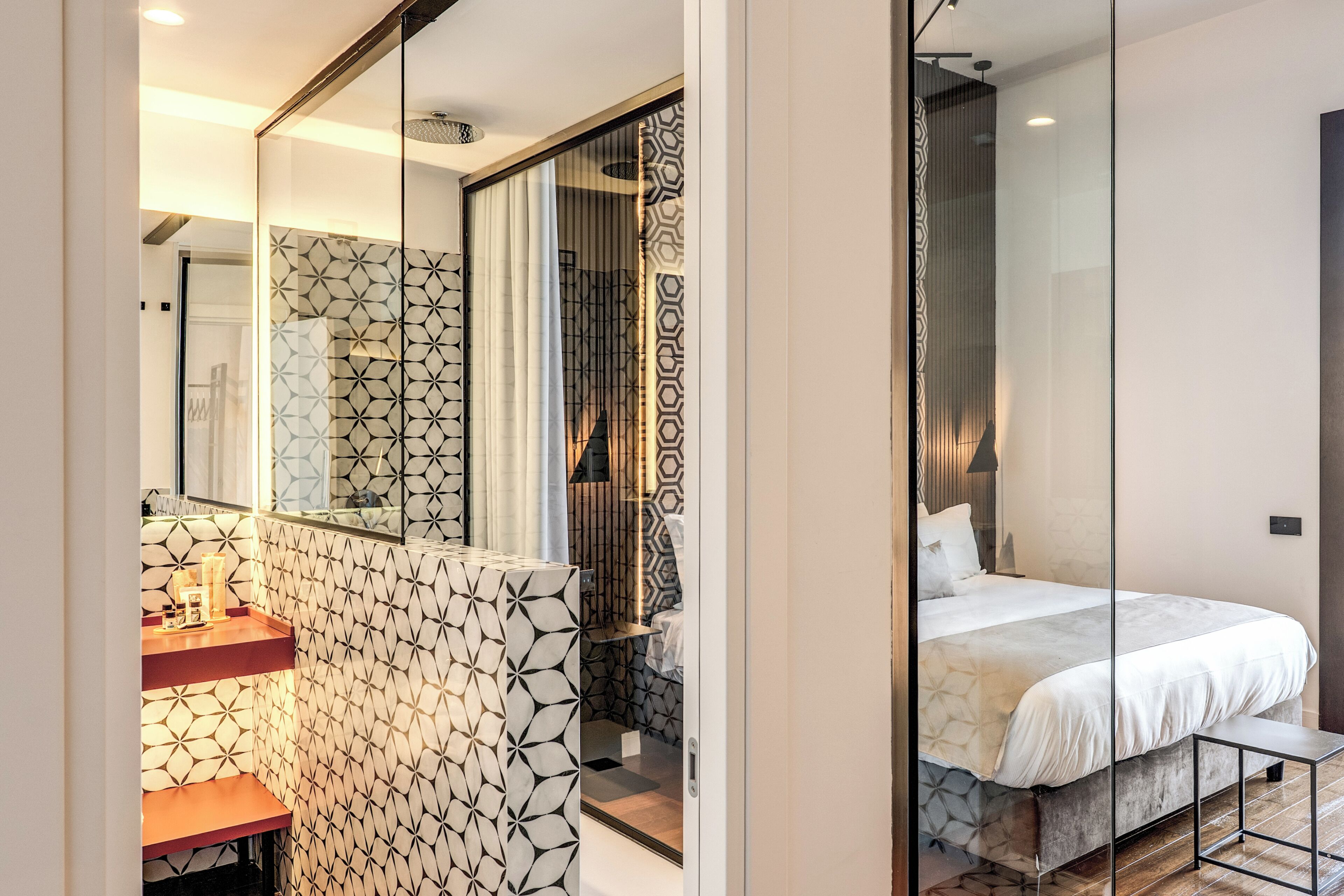 A modern bedroom with a bed, a mirror, and a bathroom with patterned tiles.