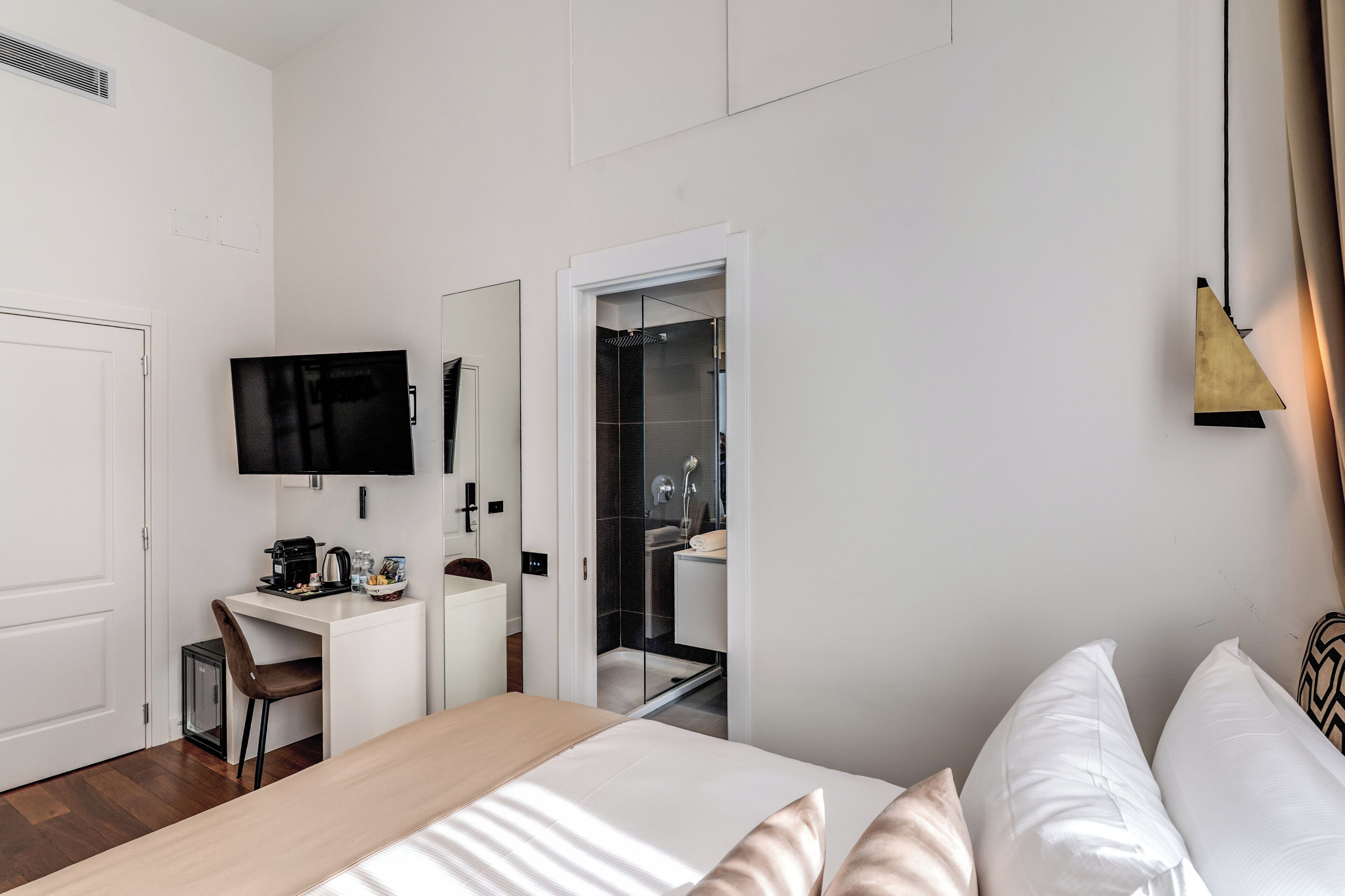 Ein Hotelzimmer mit Bett, Schreibtisch mit Kaffeemaschine, Fernseher und Duschbereich.