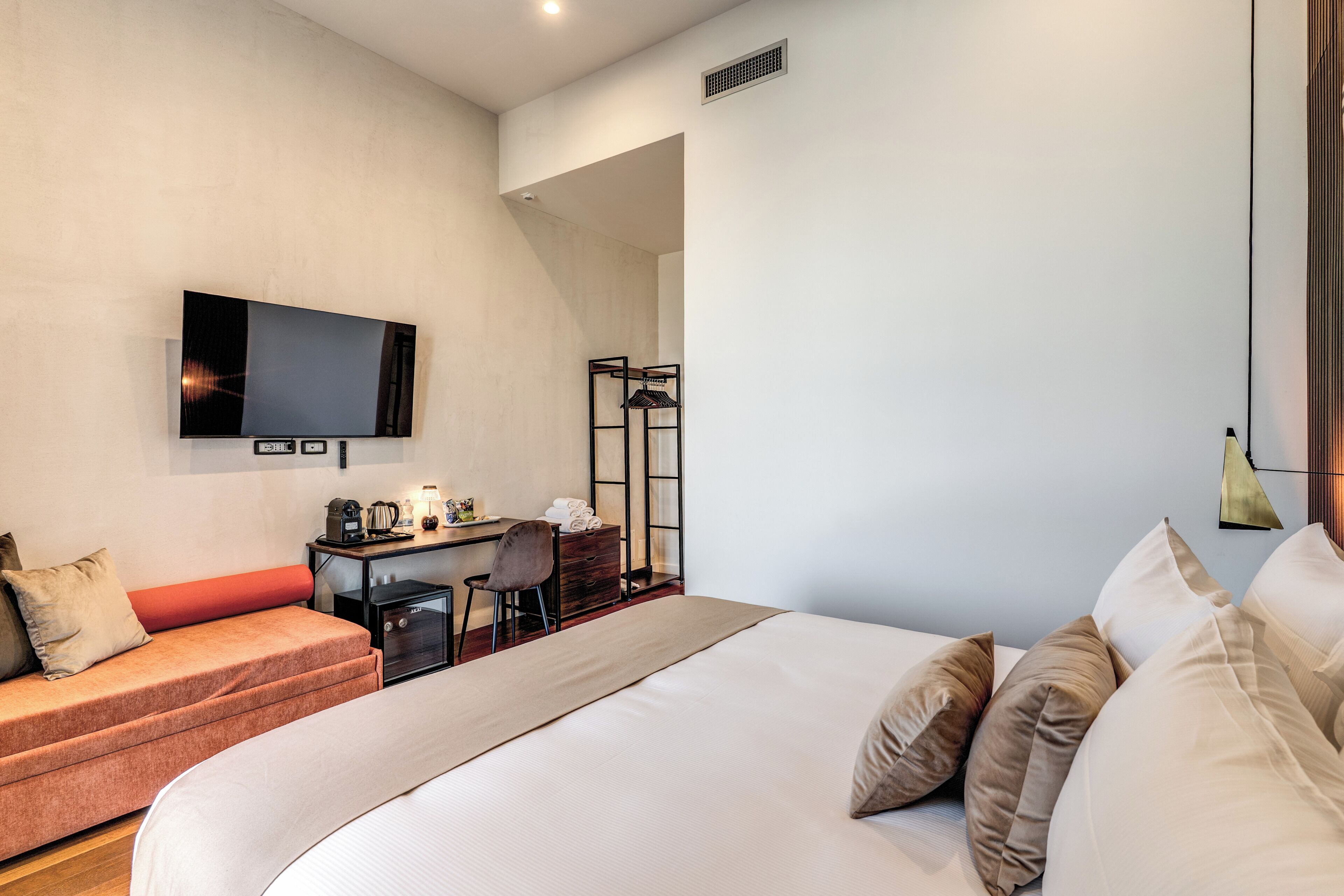 A hotel room with a bed, a sofa, a desk with a chair, a television, and a wardrobe.