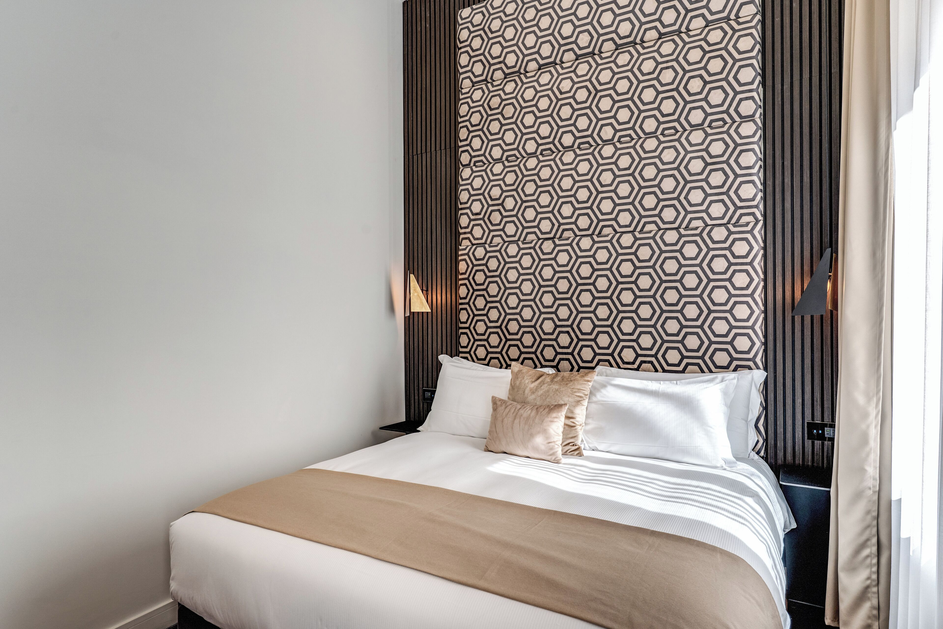 A neatly made bed with a patterned headboard, a bedside table, and a lamp.