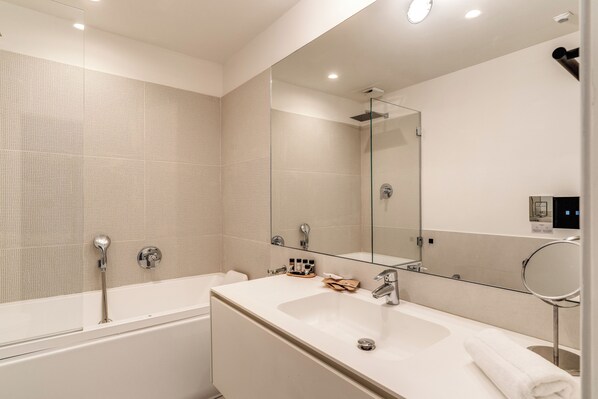 A modern bathroom with a large bathtub, a vanity with a mirror, and a shower area. - Sette Stelle Suites (Naples)
