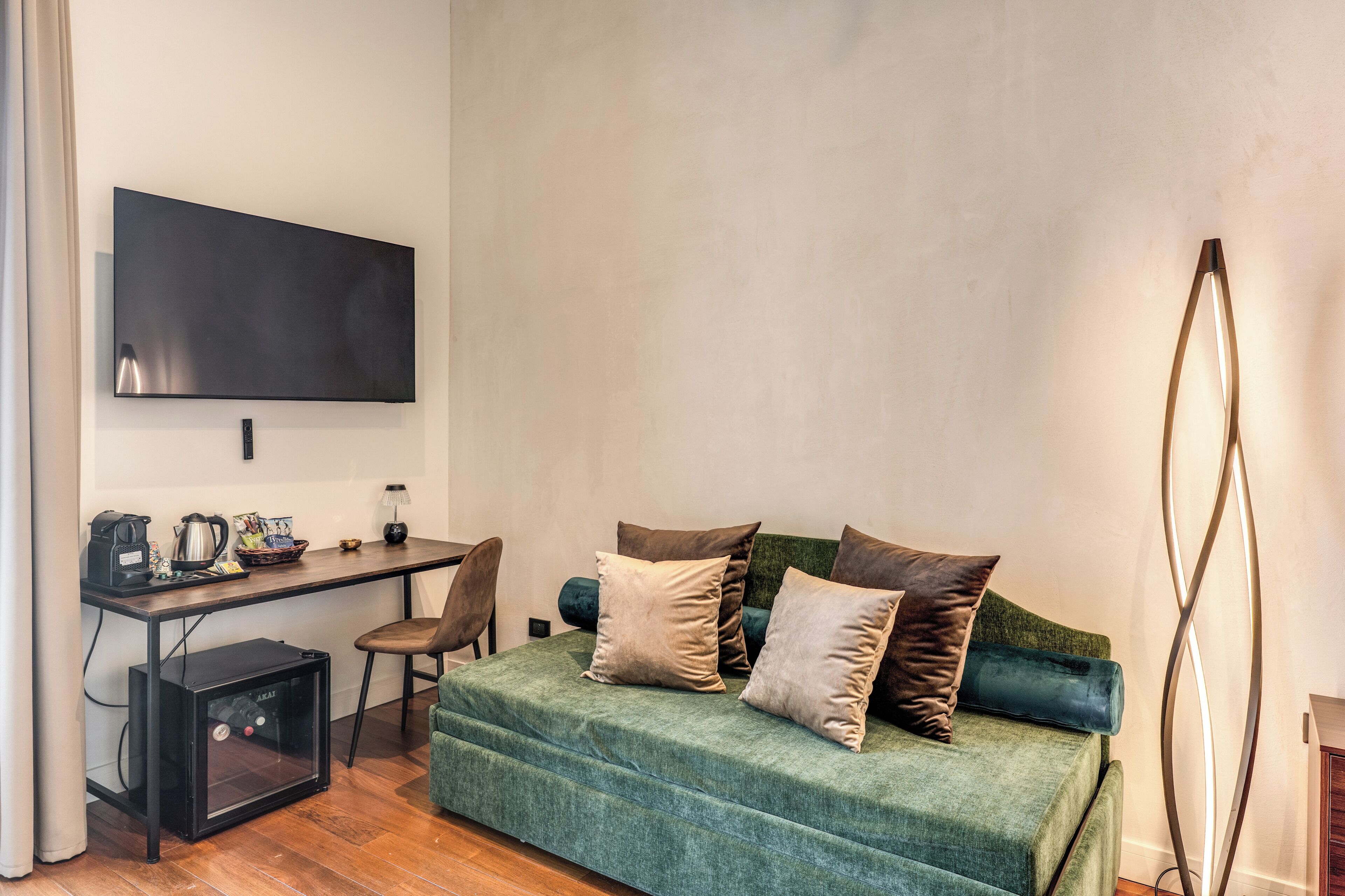 Une pièce avec un canapé vert, un bureau doté d’un téléviseur à écran plat, une machine à café et une lampe.